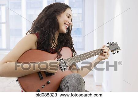 Stock Image - Mixed race woman playing guitar. Fotosearch
