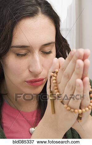 Stock Photo - Mixed race woman praying with rosary beads. Fotosearch