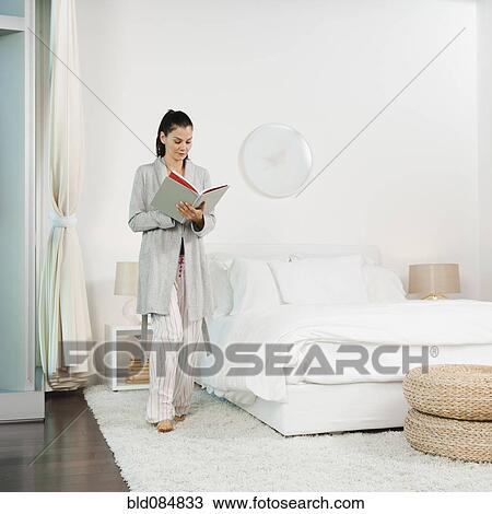 Stock Image - Mixed race woman reading book in bedroom. Fotosearch