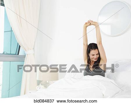 Stock Photo - Mixed race woman stretching in bed. Fotosearch