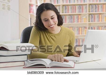 Stock Photo - Mixed race woman studying with books and laptop. Fotosearch