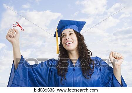 Stock Image - Mixed race woman wearing graduation cap and gown holding diploma. Fotosearch