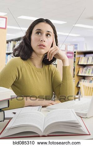Stock Image - Mixed race woman with textbooks thinking. Fotosearch