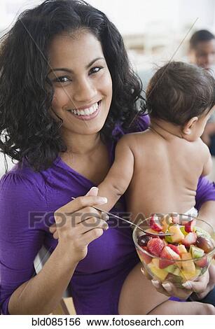 Mother holding baby and eating fruit salad View Large Photo Image Stock Photograph - Mother holding baby and eating fruit salad. Fotosearch
