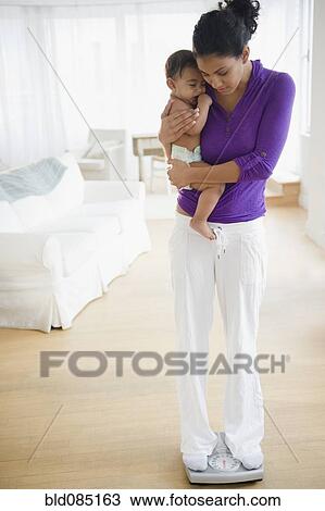 Stock Image - Mother holding baby and weighing herself. Fotosearch