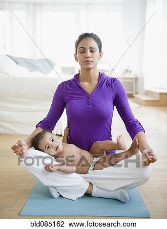 Stock Image - Mother practicing yoga with baby in lap. Fotosearch
