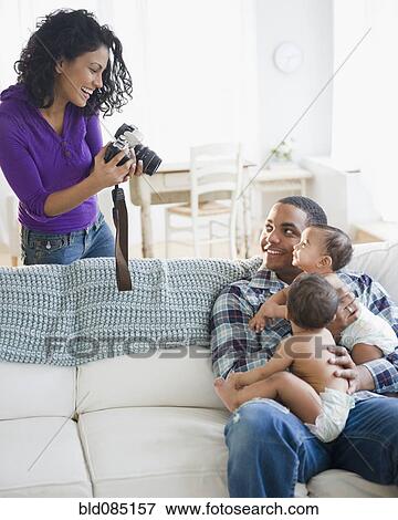 Stock Photo - Mother taking picture of father holding twin baby boys. Fotosearch