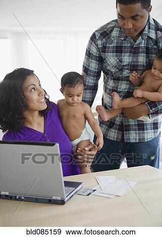 Stock Photo - Parents holding babies and paying bills online. Fotosearch