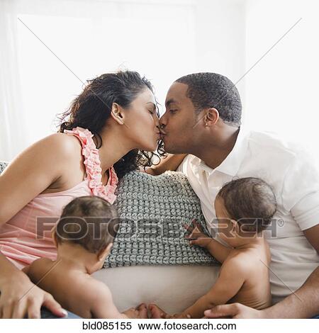 Stock Photography - Parents kissing on sofa next to twin baby boys. Fotosearch