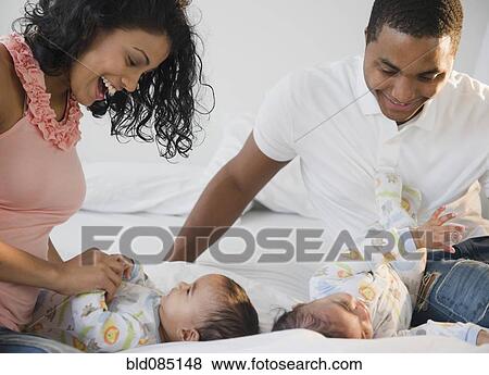Stock Photo - Parents playing on bed with baby twins. Fotosearch