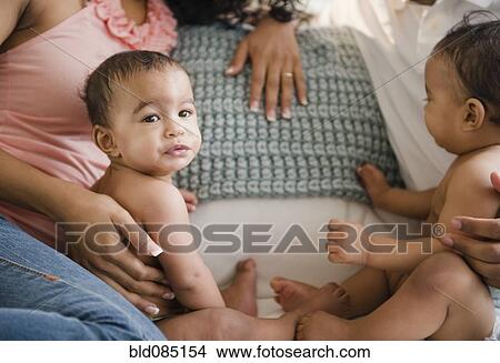 Picture - Parents sitting on sofa with twin baby boys. Fotosearch