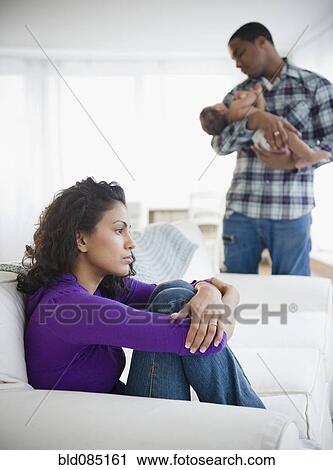 Stock Image - Sad mother with father holding baby in background. Fotosearch