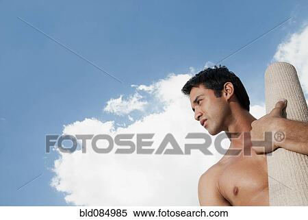 Stock Photography - Serious Hispanic man carrying yoga mat. Fotosearch