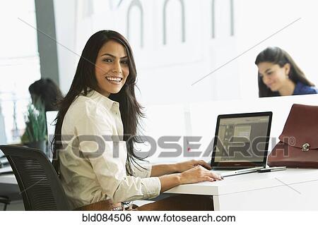 Stock Photograph - Smiling businesswoman typing on laptop in office. Fotosearch