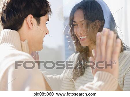 Smiling couple looking through glass at each other View Large Photo Image Stock Image - Smiling couple looking through glass at each other. Fotosearch