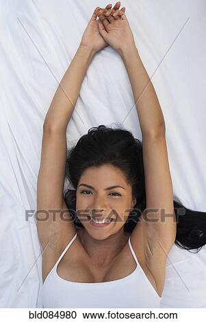 Stock Image - Smiling Hispanic woman laying in bed. Fotosearch