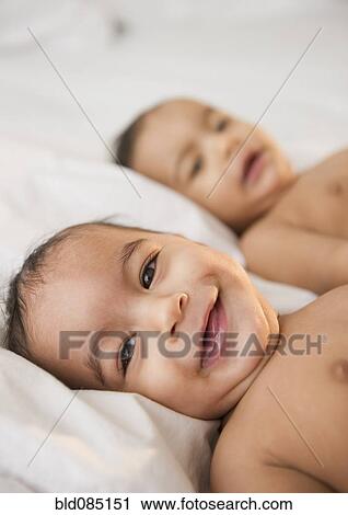 Stock Image - Smiling mixed race twins laying together. Fotosearch