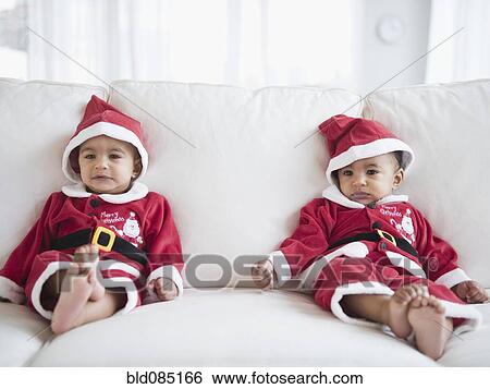 Stock Photograph - Twins on sofa dressed in Santa outfits. Fotosearch