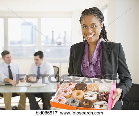 Stock Photo - African American businesswoman carrying box of donuts. Fotosearch