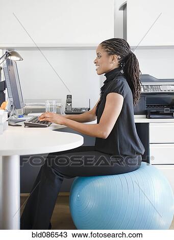 African American Woman Sitting On Exercise Ball At Desk Stock