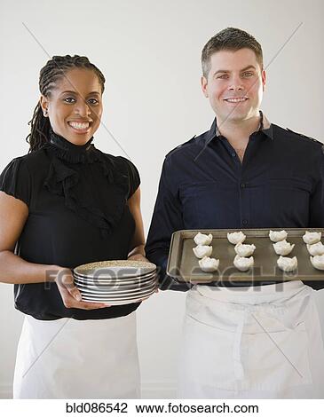 Stock Image - Caterers holding plates and tray of food. Fotosearch