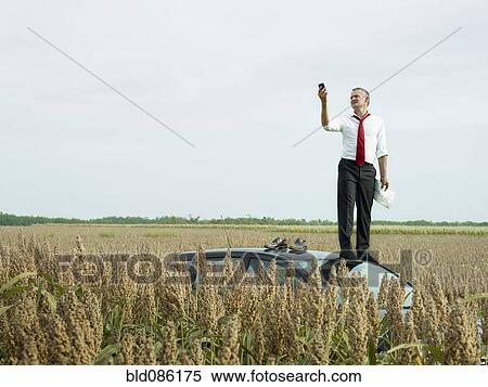 Caucasian businessman on top of car in field looking at gps device View Large Photo Image Stock Photography - Caucasian businessman on top of car in field looking at gps device. Fotosearch