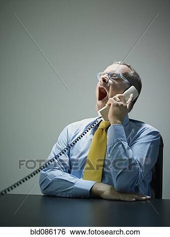 Caucasian businessman yawning and talking on telephone View Large Photo Image Stock Photograph - Caucasian businessman yawning and talking on telephone. Fotosearch