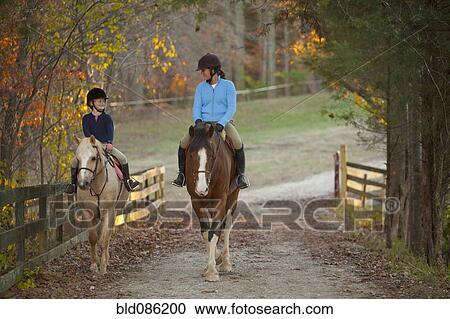 Stock Image - Caucasian girl and trainer riding horses. Fotosearch