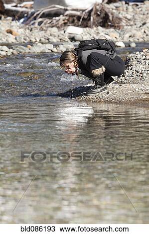 Stock Image - Caucasian hiker drinking from remote stream. Fotosearch