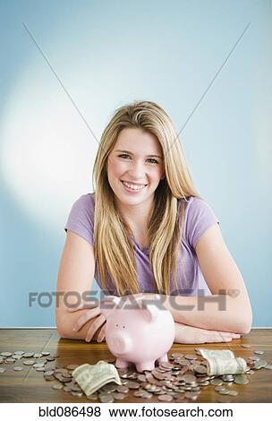 Stock Photo - Caucasian teenage girl sitting with coins and piggy bank. Fotosearch