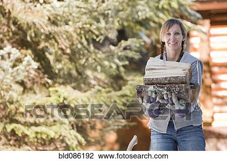 Stock Image - Caucasian woman carrying firewood. Fotosearch