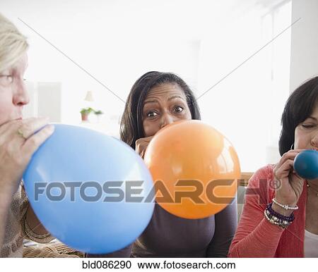 Stock Image - Friends blowing up balloons together. Fotosearch