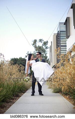 Stock Photograph - Groom carrying bride on sidewalk. Fotosearch