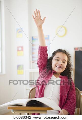 Stock Image - Hispanic girl raising hand in classroom. Fotosearch