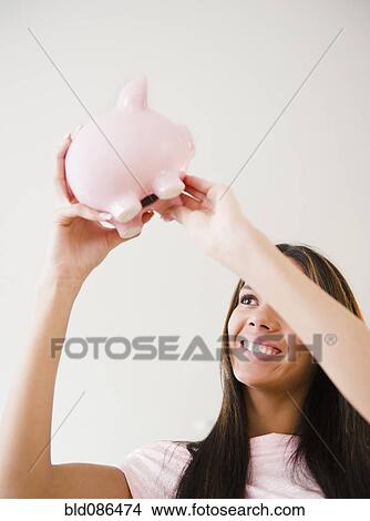 Picture - Hispanic teenage girl lifting piggy bank. Fotosearch