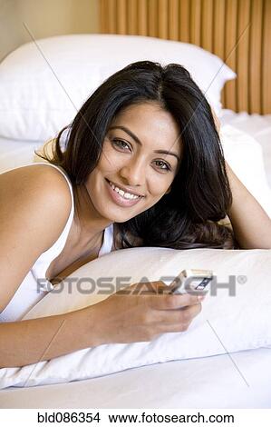 Picture - Indian woman using cell phone in bed. Fotosearch