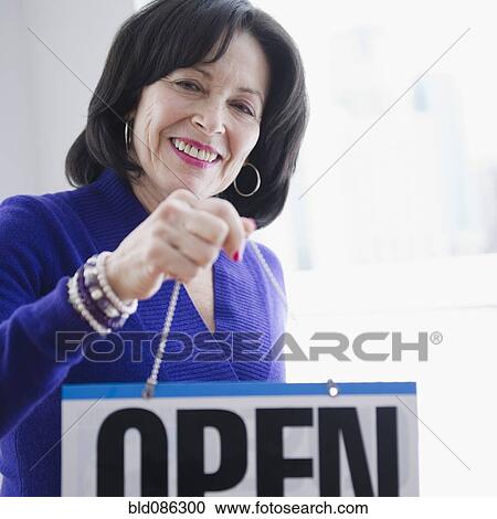 Stock Image - Mixed race woman hanging open sign. Fotosearch