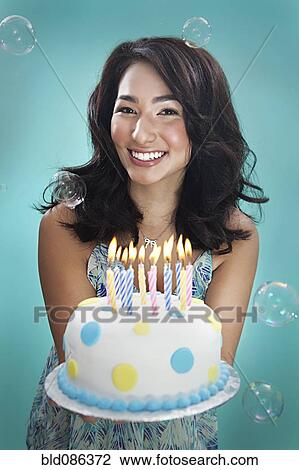 Stock Image - Mixed race woman holding birthday cake. Fotosearch