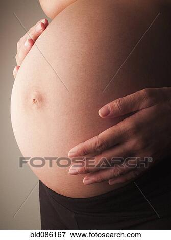 Stock Photo - Mixed race woman holding pregnant stomach. Fotosearch