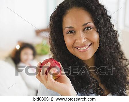 Stock Image - Mixed race woman holding red apple. Fotosearch