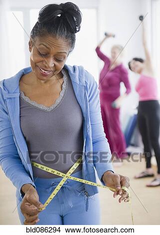 Picture - Mixed race woman measuring her waist. Fotosearch