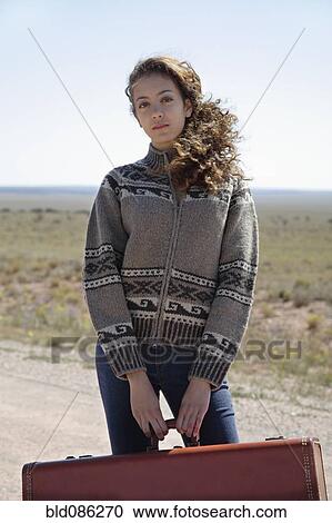 Mixed race woman standing on dirt road with suitcase View Large Photo Image Stock Image - Mixed race woman standing on dirt road with suitcase. Fotosearch