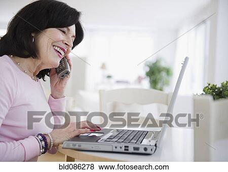 Stock Photo - Mixed race woman using laptop and talking on telephone. Fotosearch