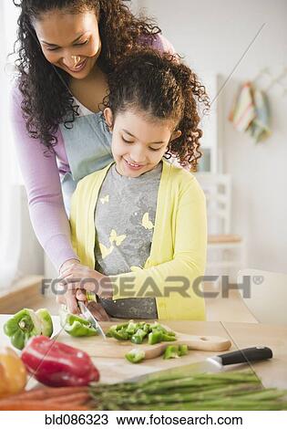 Stock Image - Mother and daughter chopping vegetables together. Fotosearch