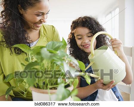 Stock Photo - Mother and daughter watering plant together. Fotosearch