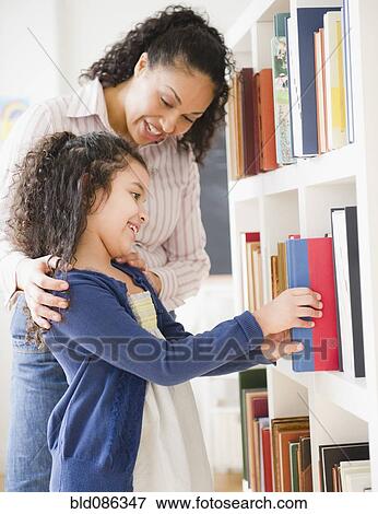 Stock Photo - Mother helping daughter choose book on shelf. Fotosearch