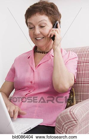 Picture - Senior Chilean woman using laptop and cell phone. Fotosearch