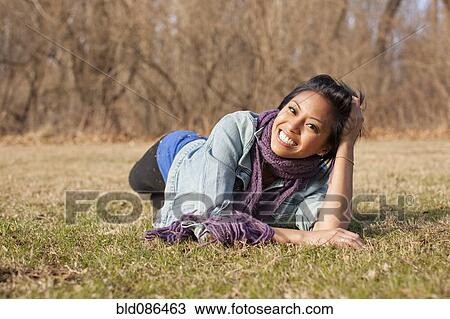 Stock Image - Smiling Asian woman laying in grass. Fotosearch