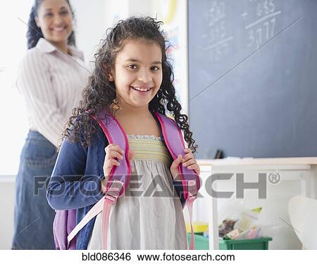 Stock Photograph - Smiling Hispanic girl with backpack in classroom. Fotosearch