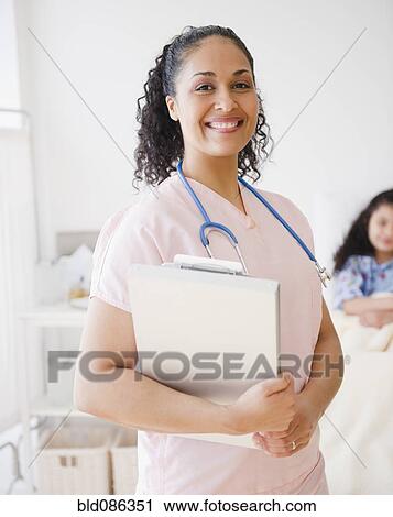 Stock Image - Smiling mixed race nurse in hospital room. Fotosearch